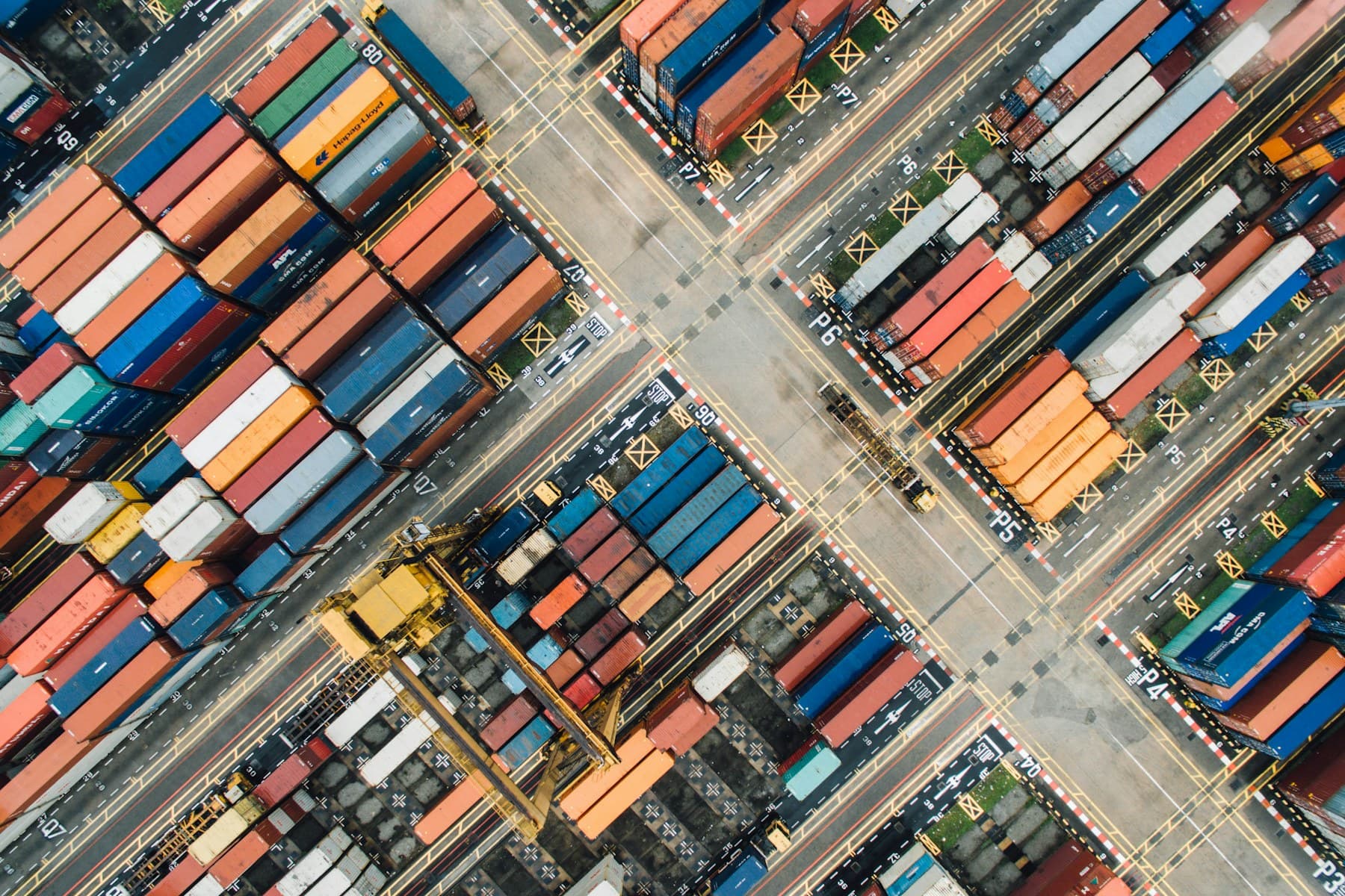 An aerial view of a container yard, coloured containers arranged in precise diagonal rows.